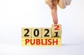 Symbol of planning 2022 publish new year. Businessman turns a wooden cube and changes words `publish 2021` to `publish 2022`.