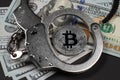 Symbolic coins of bitcoin and stack of bitcoin coins and metall handcuffs on banknotes of one hundred dollars