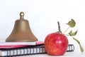 Symbols for education, red delicious homegrown apple, brass school bell stacked on black spiral bound sketch notebook, red folder Royalty Free Stock Photo
