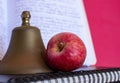 Symbols for education, red delicious homegrown apple, brass school bell stacked on black spiral bound sketch notebook, red folder Royalty Free Stock Photo