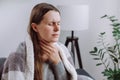 Symptoms from flu season in winter concept. Close-up of unhealthy sad young woman covered blanket sitting on grey couch at home Royalty Free Stock Photo