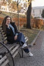 Syoung woman sitting on bench in park talking on phone. Young woman uses smartphone. Vertical frame Royalty Free Stock Photo