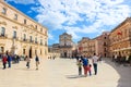 Syracuse, Sicily, Italy - Apr 10th 2019: Tourists walking on the Piazza Duomo Square. Beautiful Santa Lucia Alla Badia Church