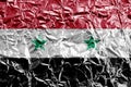 Syria flag depicted in paint colors on shiny crumpled aluminium foil closeup. Textured banner on rough background