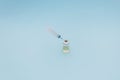 A syringe and a can of vaccine stand on a blue background, minimalism