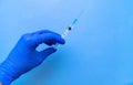 A syringe containing the coronavirus vaccine is held by a blue-gloved hand on a blue background in close-up. Royalty Free Stock Photo