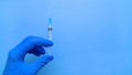 A syringe containing the coronavirus vaccine is held by a blue-gloved hand on a blue background in close-up. Royalty Free Stock Photo
