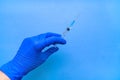 A syringe containing the coronavirus vaccine is held by a blue-gloved hand on a blue background in close-up. Royalty Free Stock Photo