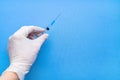 A syringe containing the coronavirus vaccine is held by a white-gloved hand on a blue background in close-up. Space for text. Royalty Free Stock Photo