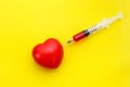 Syringe give medicine to red heart shape on yellow background. U
