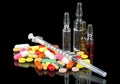 Syringe with glass vials and medicinal tablets and pills on black background. Assorted medical drugs