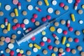 Syringe for injection on a blue background surrounded by different pills