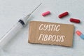 Syringe injection, pill capsules and brown card with text CYSTIC FIBROSIS