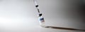 The syringe is stuck in the cap of a glass tilted bottle with a transparent covid vaccine