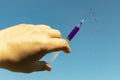 Syringe with medicine in hand and drops against the blue sky