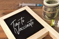 Syringe, money banknotes and chalkboard written with TIME TO VACCINATE