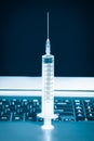 Syringe next to a laptop computer toned in blue Royalty Free Stock Photo