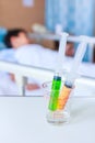 Syringes in a glass measuring cup with blurred illness boy lying