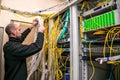 The system administrator is laying new cable communications in server racks. The man switches the wires to the cross panel of the Royalty Free Stock Photo