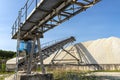 A system of interconnected conveyor belts over heaps of gravel against a blue sky at an industrial cement plant.