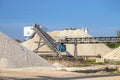 A system of interconnected conveyor belts over heaps of gravel against a blue sky at an industrial cement plant.