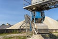 A system of interconnected conveyor belts over heaps of gravel against a blue sky at an industrial cement plant.