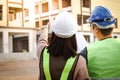 System architects and system engineers stand looking at the blueprints at the building construction site.