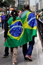 Couple holding hands and the Brazilian flag on their back walking along Paulista avenue