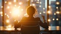 Back view of a person seated at a desk in a dimly lit office, facing a large window. Royalty Free Stock Photo