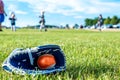 T-ball resting inside a baseball glove on grass. Defocused players in background