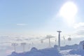 T-bar and gondola lifts emerge through and above the clouds. Photo into the bright sun