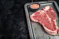 T-bone steak, raw marbled beef meat in a steel kitchen tray with herbs. Black background. Top view. Copy space Royalty Free Stock Photo