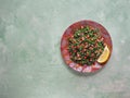 Tabbouleh salad, plate, concrete background. Levantine vegetarian salad with parsley, mint, bulgur, tomato.