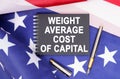 On the table is an American flag, a pen and a notebook with the inscription - WEIGHT AVERAGE COST OF CAPITAL