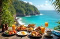 Table with assorted breakfast dishes, orange juice set against backdrop of tropical ocean cliffside view. Fresh fruit, eggs, Royalty Free Stock Photo