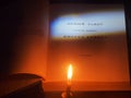 On the table is a book on which the inscription "Holy Bible" in Russian is illuminated. A candle is burning next to it Royalty Free Stock Photo