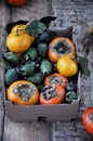 On the table in a box a fresh persimmon, feijoa and citrus mandarins