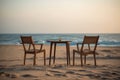 A table and chairs on the beach at sunset, created by Generative AI Royalty Free Stock Photo
