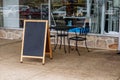 Table chairs and a blank chalkboard sign outside in front of the glass window of a restaurant. Royalty Free Stock Photo
