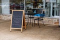 Table chairs and chalkboard sign outside in front of the glass window of a restaurant,