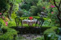 A table and chairs placed in the middle of a garden, surrounded by greenery and flowers, An elegant dining table for two amidst a Royalty Free Stock Photo