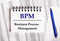 On the table are charts and reports, on which lie a blue pen and a notebook with the word BPM Business Process Management