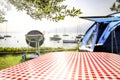 Table with checkered tabletop and blurred grill on grass and garden and lake background. Royalty Free Stock Photo