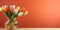 Table with colorful tulips in glass vase against orange wall. Interior background with copy space Royalty Free Stock Photo