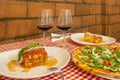 Table in the dining room of an Italian restaurant with pizza to share and individual plates of lasagna and two glasses of red wine