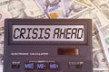 On the table are dollars and a calculator on the electronic board which says CRISIS AHEAD