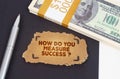 On the table are dollars, a pen and a cardboard sign with the inscription - HOW DO YOU MEASURE SUCCESS