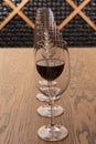 On the table empty wine glasses stand in a row, one wine glass with wine, on the background of a rack with many bottles Royalty Free Stock Photo