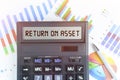 On the table are financial charts and a calculator, on the electronic board of which is written the text - RETURN ON ASSET