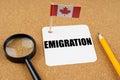 On the table is the flag of Canada, a pencil, a magnifying glass and a sheet of paper with the inscription - Emigration